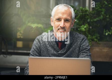 Its my favourite place to get a little work done. Portrait of a mature businessman using his laptop in a cafe. Stock Photo