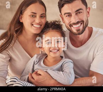 Happy family, girl and an interracial couple smiling and excited about spending quality time together. Portrait of parents, mother and father having fun with their adopted daughter at home Stock Photo