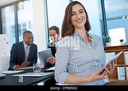 Success is the reason for my smile. Portrait of a young businesswoman working in the boardroom with her colleagues in the background. Stock Photo