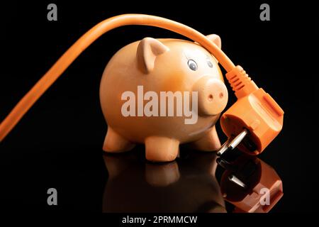 Orange electric plug and piggy bank on black background. Concept of increasing electricity prices. Stock Photo