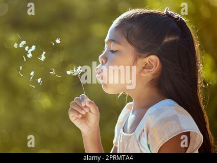 Spring, freedom and girl blowing dandelion flowers for hope, growth and environment in park. Happy, light and health with child wish on plant in peace Stock Photo