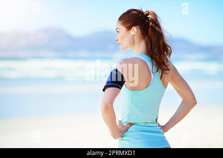 Taking it all in. a young woman standing with her hands on her hips on the beach. Stock Photo