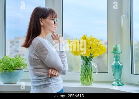Middle-aged serious pensive woman looking out the window. Stock Photo