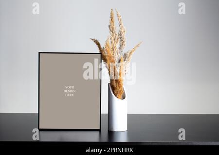 Poster mockup black photo frame on the black wooden table with beautiful dry plant in white vase and white wall Stock Photo