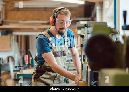 Absorbed carpenter with ear protection and safety goggles at the milling machine working on wood Stock Photo