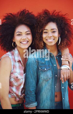 Best friends are like unbiological sisters. two young friends posing against a red background. Stock Photo