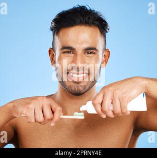 Mouth, dental and man brushing teeth in studio for wellness, health and grooming on blue background. Portrait, face and teeth of indian guy happy with Stock Photo