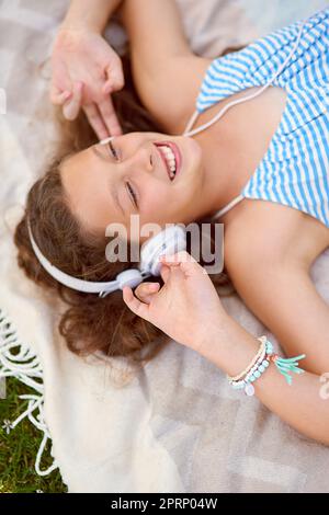 Getting lost in the music. High angle shot of a young girl listening to music while lying on a blanket outside. Stock Photo