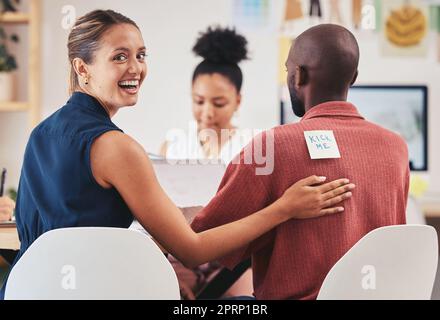 Comic or funny business woman april fools prank or joke with coworker with paper note or sign on his back in corporate office. Smile, happy and joke or laugh and working at desk in corporate company Stock Photo