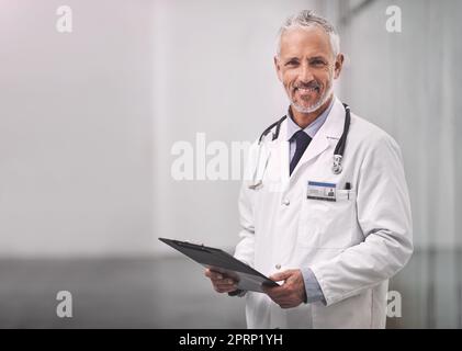Here to help guide you to good health again. Portrait of a mature male doctor standing with a clipboard in a hospital. Stock Photo