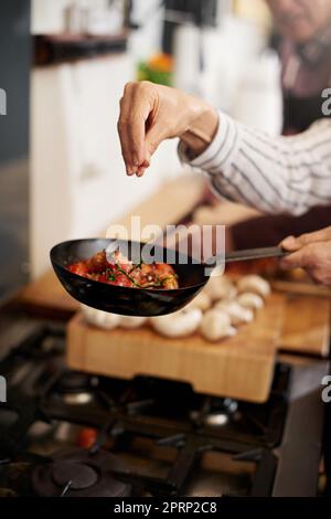 The missing ingredient. a unrecognizable persons hand adding salt to a pan of tomatoes in the kitchen. Stock Photo