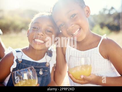 Juice, vitamin c and happy children on picnic in summer or portrait in green park, garden or outdoor holiday vacation. Youth, wellness and happy kids drinking healthy fruit drink lens flare and smile Stock Photo