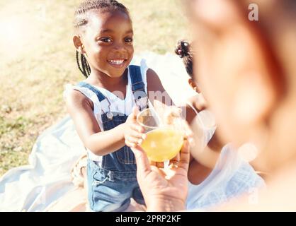 Happy girl, juice and smile in family picnic fun and joy in happiness on a warm summer day in nature. Black child smiling for fresh cold healthy beverage in the hot outdoors with parent and sibling Stock Photo
