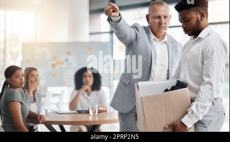 Black man, sad and fired by boss in a meeting holding a box in disappointment at the office. Manager or company leader pointing to the exit and firing employee in front of colleagues at the workplace Stock Photo