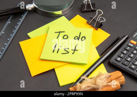 bottom close view to do list written on sticky note colorful sticky notes lupa pen calculator cinnamon sticks ruler on dark background Stock Photo