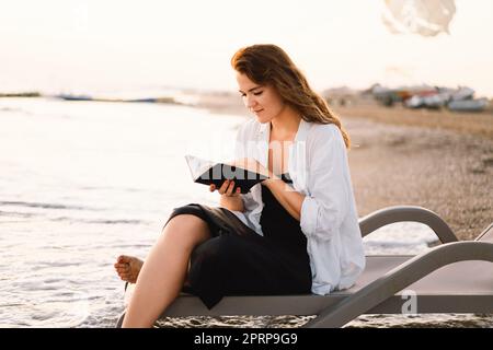 Christian woman holds bible in her hands. Reading the Holy Bible on the sea during beautiful sunset Stock Photo