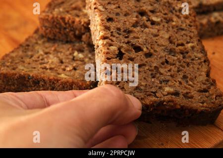 Woman's hand taking whole grain bread, close-up. Healthy food concept. Defocus. Stock Photo