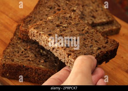 Woman's hand taking whole grain bread, close-up. Defocus. Healthy food concept. Stock Photo