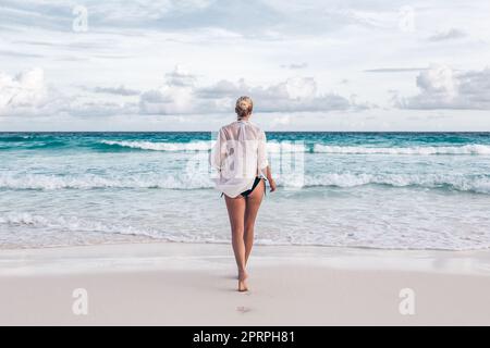 Woman wearing white loose tunic over bikini on Mahe Island, Seychelles. Summer vacations on picture perfect tropical beach concept. Stock Photo