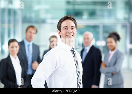 I know Im going to succeed in my career. Attractive young business associate smiling with his colleagues in the background - portrait. Stock Photo