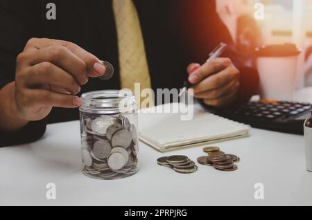 Man hand putting money coin and take note of income and expenses and working to save money for the future growing business, education and retirement. Stock Photo