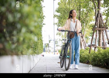 Happy female smiling walk down the street with her bike on city road Stock Photo