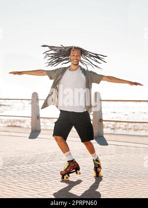 Training, sports and skate with a man roller skating on the promenade by the beach with the sea in the background. Fitness, fun and freedom with a young male on roller skates outside in summer Stock Photo