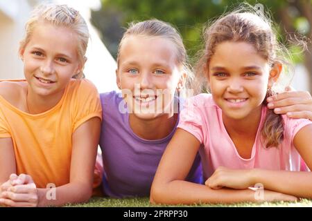 Best friends for life. Portrait of three girls lying on the grass on a sunny afternoon smiling at you. Stock Photo