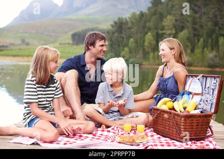Fresh air and family time. Cute young family sitting picnicking on a jetty near the lake. Stock Photo
