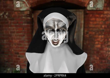 Portrait of scary devilish nun near red brick wall. Halloween party look Stock Photo