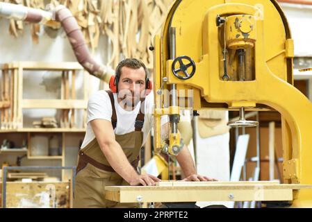 portrait of a carpenter in work clothes and hearing protection in the workshop of a carpenter's shop Stock Photo