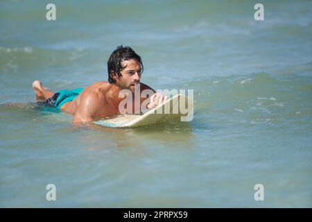 Waiting for the next big wave. An attractive young man waiting for a wave on his board in the ocean. Stock Photo