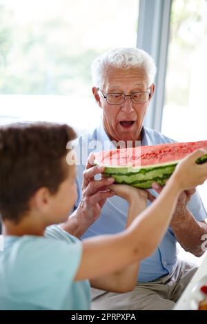 For me. a little boy handing his grandfather a slice of watermelon. Stock Photo