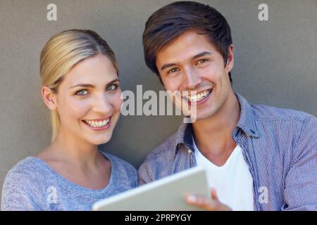 It works for us and itll work for you. Portrait of a happy young couple using a digital tablet together against a gray background. Stock Photo