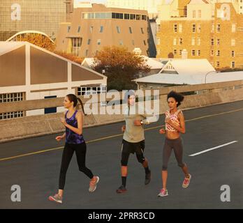 We love the quiet of a morning run. three joggers running down an empty highway in the morning. Stock Photo
