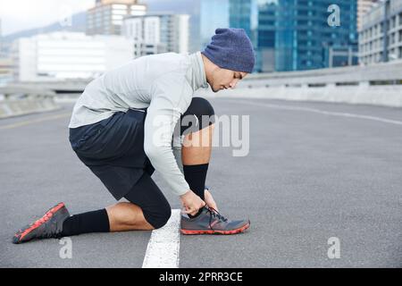 Last minute prep before running. a young man tying up his shoelaces before a run through the city. Stock Photo