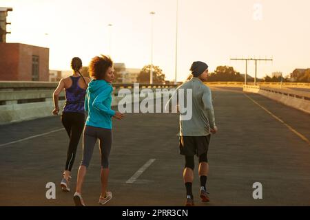 This early, it is we who own the street. Rearview shot of three young joggers running down an empty street at dawn. Stock Photo