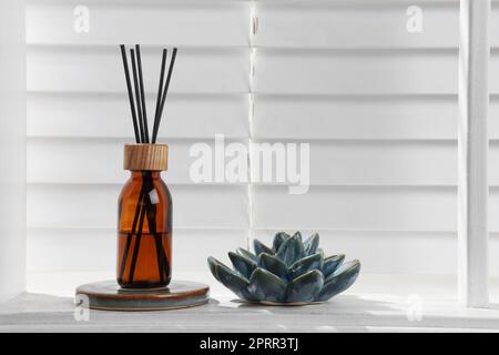 Air reed freshener and ceramic decor on white table near window. Space for text Stock Photo