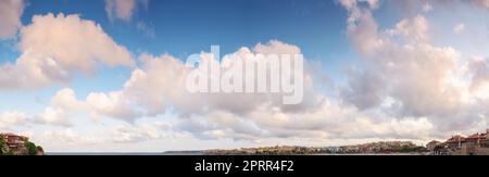 panorama with fluffy clouds on a blue sky in evening light. beautiful nature background at the sea. warm weather in velvet season Stock Photo