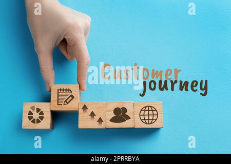 Woman arranging wooden cubes with different images on light blue background, top view. Customer journey concept Stock Photo