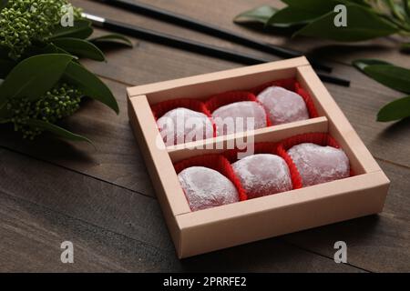 Box of delicious mochi and leaves on wooden table. Traditional Japanese dessert Stock Photo