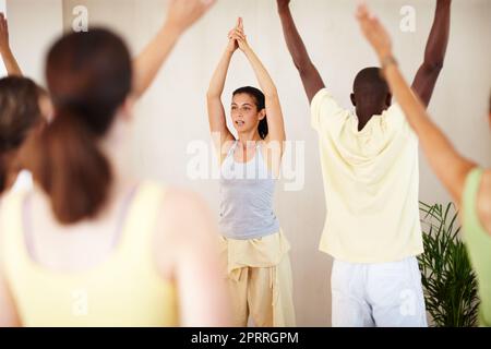 Experienced instructor leading her class. A pretty yoga instructor showing her class how to perform a routine. Stock Photo