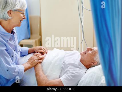 The reassuring touch of love. a senior woman comforting her sick husband who is lying in a hospital bed. Stock Photo