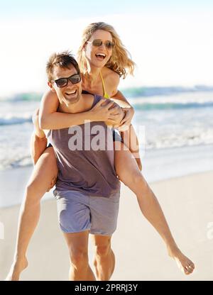 Im there when she needs a lift. a laughing couple looking blissful as man carries woman on his back. Stock Photo