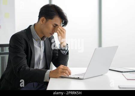 Young asian businessman in black suit massages between eyes with fingers. The concept of unemployed, sadness, depressed and human problems. Stock Photo