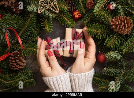 Female hands holding two gift boxes on a wooden table near Christmas decorations top view Stock Photo