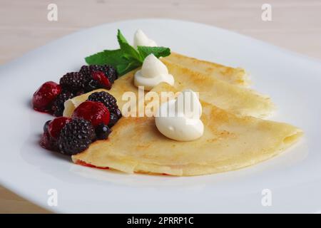 Portion on thin pancakes with sweet cream cheese and berries. Stock Photo