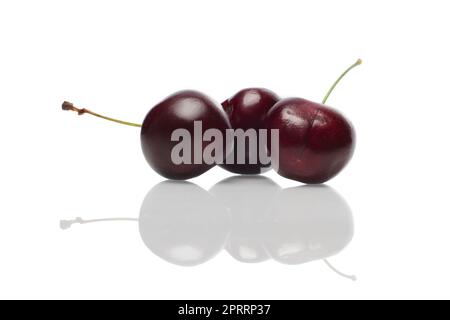 Three fresh cherries with reflection on glossy surface. Stock Photo