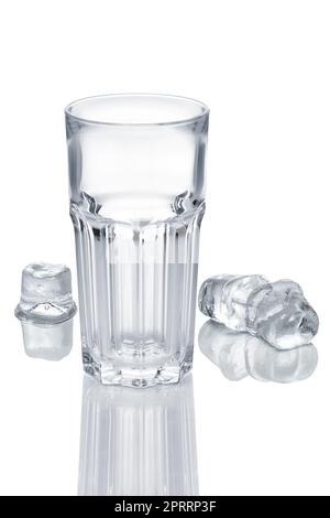 Empty faceted glass and three ice cubes melting on white glass table Stock Photo