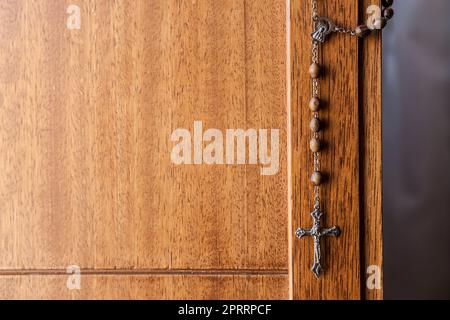 Catholic rosary hanging from wooden door. Selective focus Stock Photo